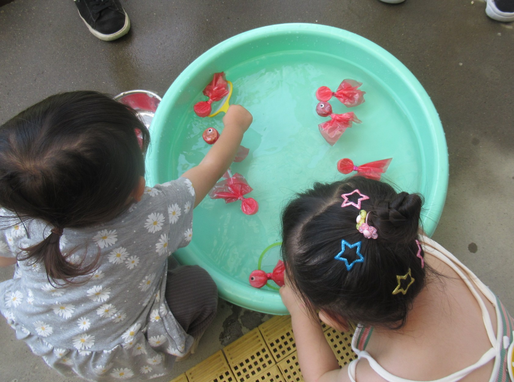 2人の女の子が製作物の金魚すくいをしている画像です